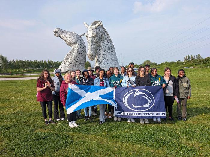 Students with a flag in front of twin horse statues